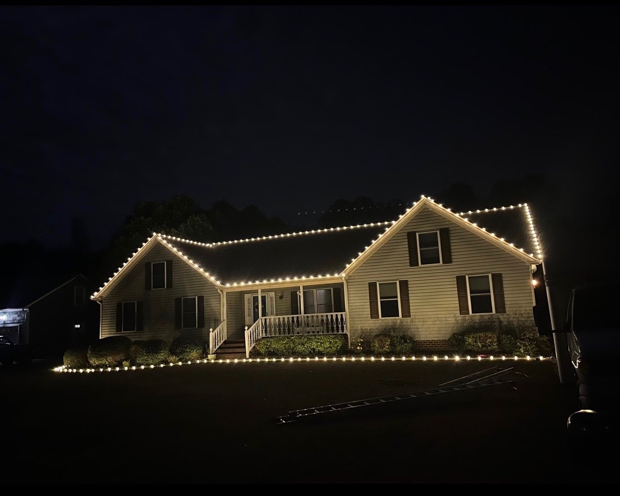 Residential roofline and porch wrapped in warm white holiday lights at night