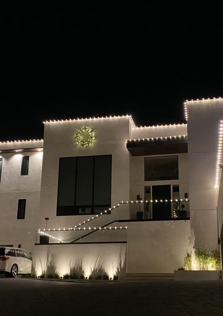 Modern white facade traced in warm white lights with a lit wreath and path lighting