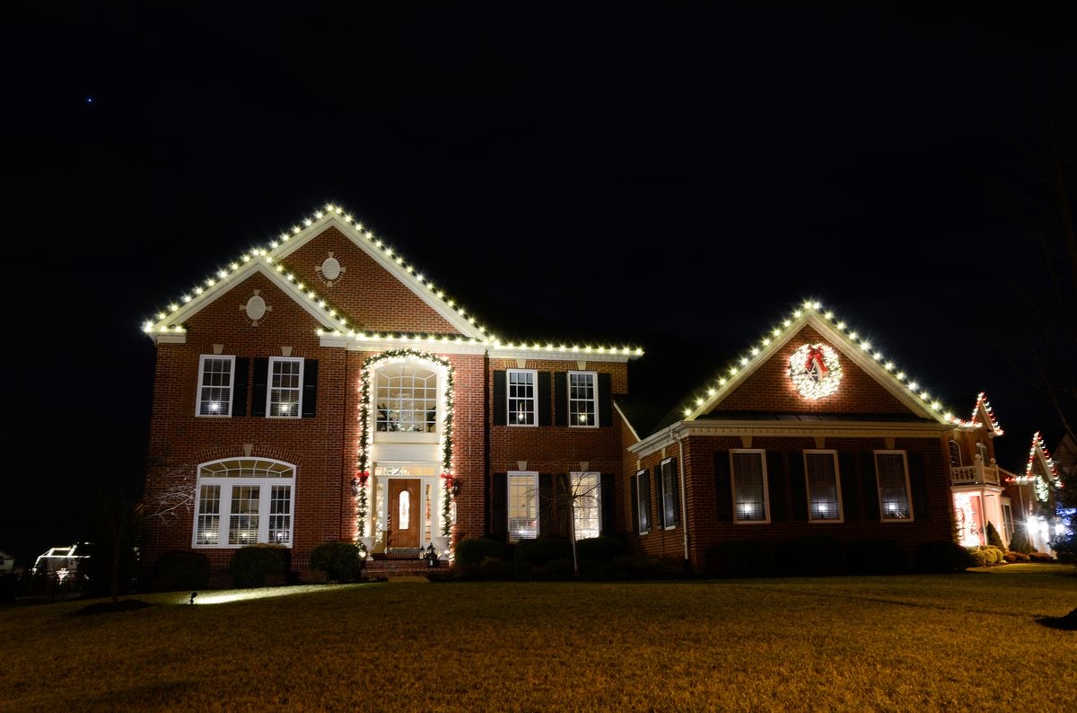 Brick home with lit roofline, garland and glowing wreath at night